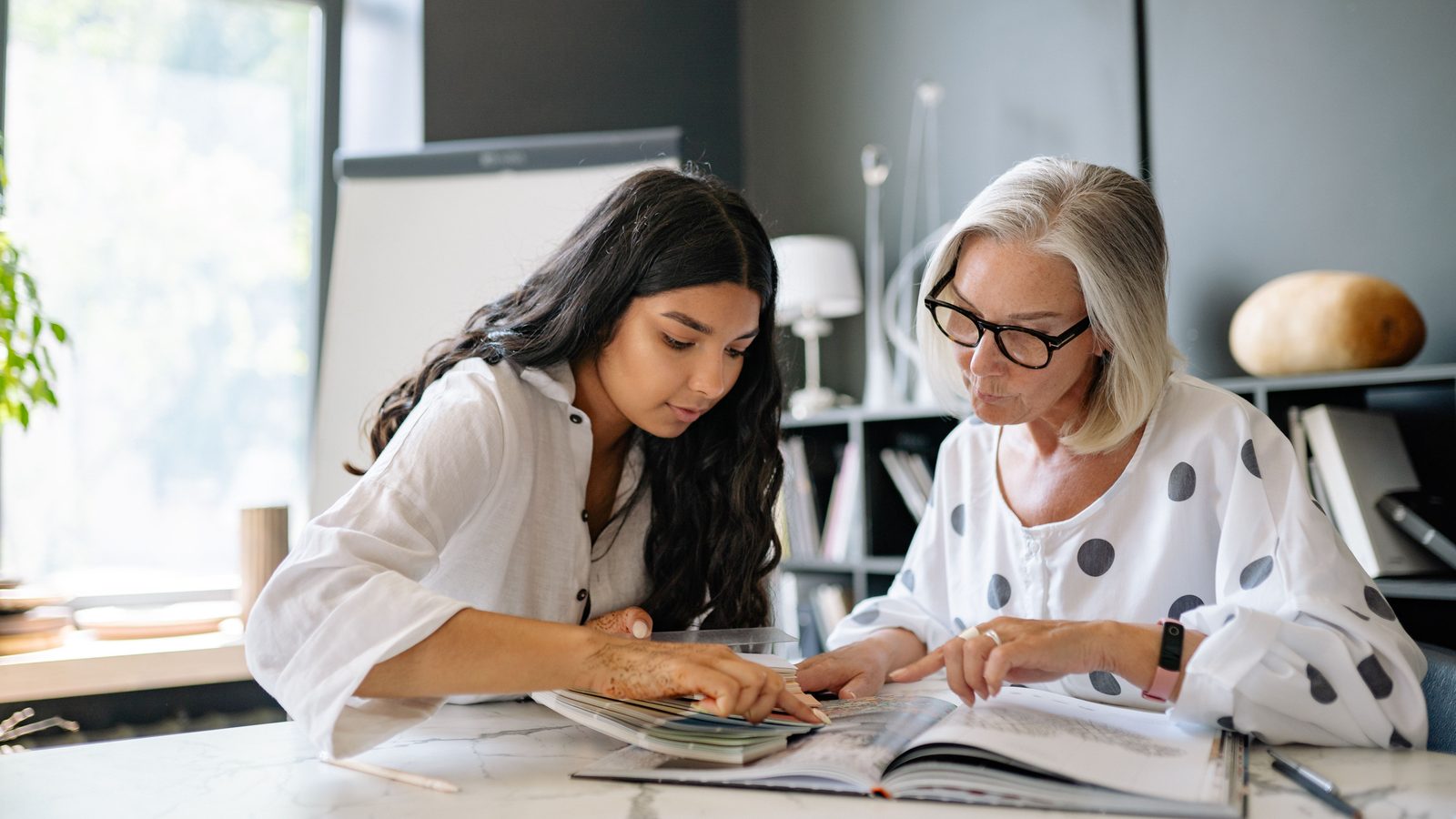 An experienced colleague reviewing documents with a younger coworker at a table.